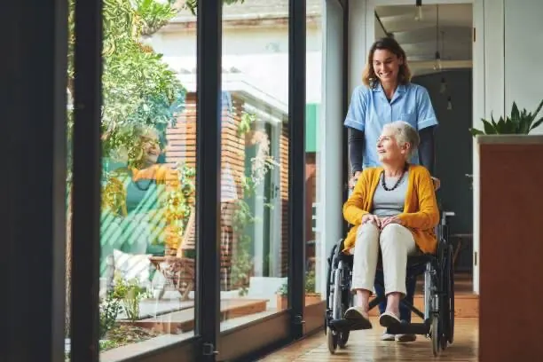 Une soignante accompagne une résidente en fauteuil roulant dans un couloir lumineux